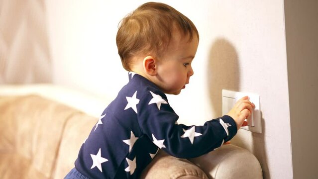 Baby boy in blue shirt with white stars at the light switch. Little kid turns the light on and off.