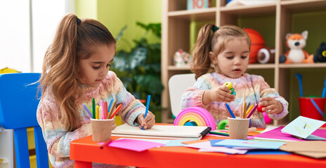 Two kids preschool students sitting on table drawing on paper at kindergarten