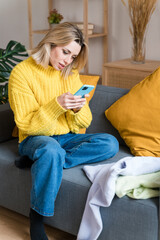 Obraz premium Young woman using smartphone on sofa taking pictures of her clothes