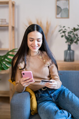 Smiling woman using smartphone at home shopping online