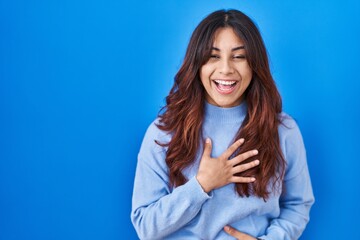 Hispanic young woman standing over blue background smiling and laughing hard out loud because funny crazy joke with hands on body. - obrazy, fototapety, plakaty