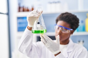 African american woman wearing scientist uniform measuring liquid at laboratory