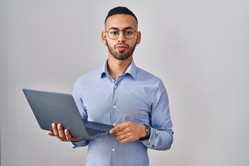 Young hispanic man working using computer laptop looking at the camera blowing a kiss on air being lovely and sexy. love expression.