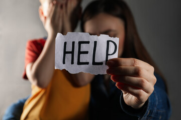 Little boy and mother holding piece of paper with word Help against light grey background, focus on hand. Domestic violence concept