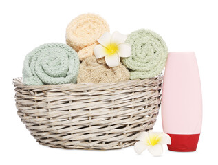 Fototapeta na wymiar Soft towels in wicker basket, bottle of cosmetic product and plumeria flowers on white background