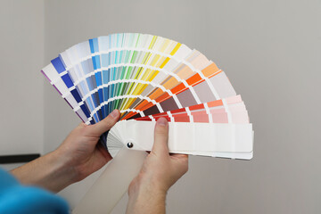 Man with palette choosing color for painting wall indoors, closeup. Interior design