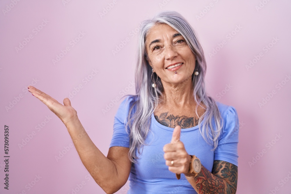 Sticker middle age woman with tattoos standing over pink background showing palm hand and doing ok gesture w