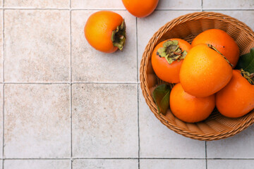 Delicious ripe juicy persimmons in wicker basket on tiled surface, flat lay. Space for text