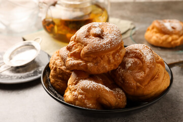 Delicious profiteroles with powdered sugar in bowl on grey table