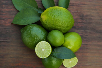 Whole and cut fresh ripe limes with green leaf on wooden table, flat lay