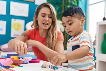Fototapeta premium Teacher and toddler playing with geometry blocks sitting on table at kindergarten