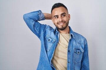 Young hispanic man standing over isolated background smiling confident touching hair with hand up gesture, posing attractive and fashionable