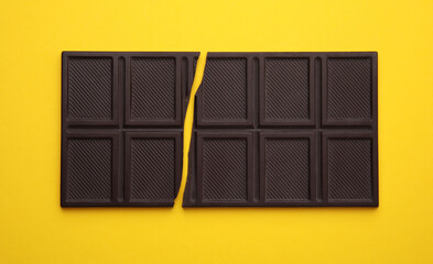Broken chocolate bar on yellow background, top view