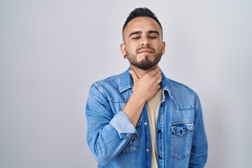 Young hispanic man standing over isolated background touching painful neck, sore throat for flu, clod and infection