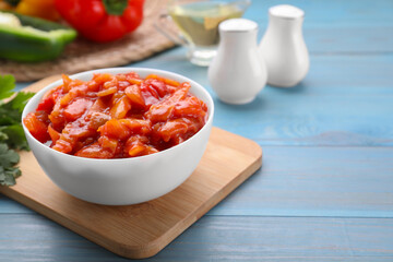 Bowl of delicious lecho on light blue wooden table, closeup. Space for text