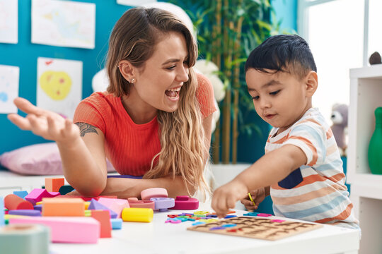 Teacher and toddler playing with maths puzzle game sitting on table at kindergarten