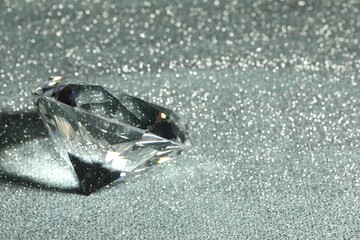 Beautiful dazzling diamond on silver glitter background, closeup. Space for text