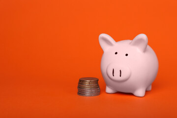 Ceramic piggy bank and coins on orange background, space for text. Financial savings