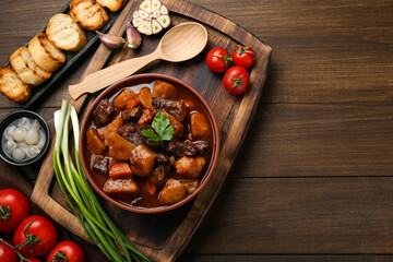 Delicious beef stew with carrots, parsley and potatoes on wooden table, flat lay. Space for text