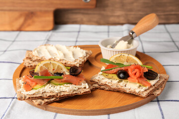 Fresh crunchy crispbreads with cream cheese, salmon, olives, lemon and green onion on table