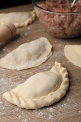 Uncooked chebureki, minced meat and rolling pin on wooden table