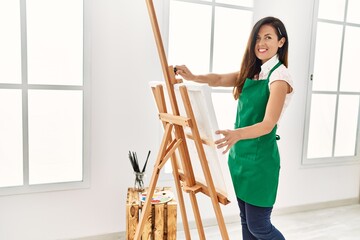Middle age hispanic woman smiling confident looking canvas draw at art studio