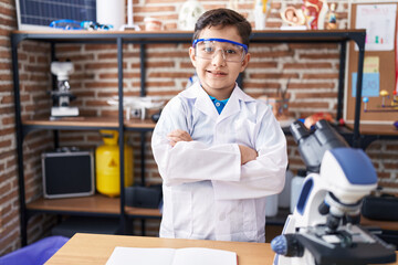 Fototapeta na wymiar Adorable hispanic boy student smiling confident standing with arms crossed gesture at laboratory classroom