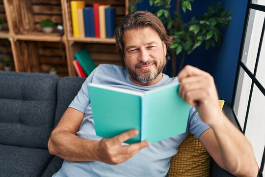 Middle age man reading book sitting on sofa at home