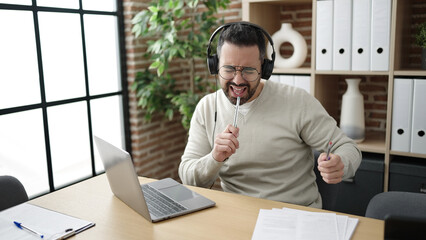 Young hispanic man business worker listening to music doing drummer gesture at office