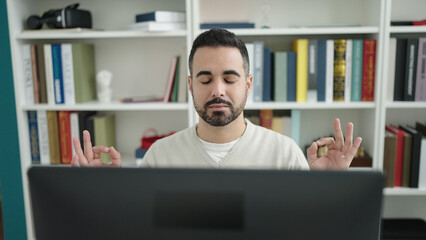 Young hispanic man student doing yoga exercise at library university