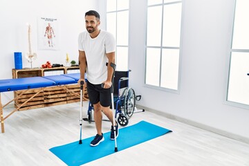 Young hispanic man patient having rehab session walking using crutches at clinic - Powered by Adobe