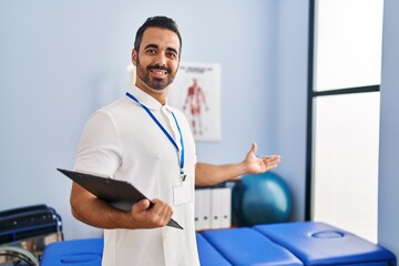 Naklejka na ściany i meble Young hispanic man physiotherapist smiling confident holding clipboard at rehab clinic
