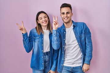 Young hispanic couple standing over pink background smiling with happy face winking at the camera...