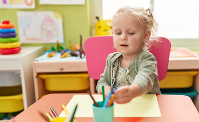 Adorable blonde girl preschool student sitting on table drawing on paper at kindergarten