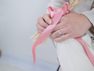 Groom hands wearing rings sitting on chairs holding bouquets.