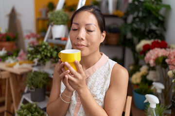 Young asian woman florist smiling confident drinking cup of coffee at flower shop