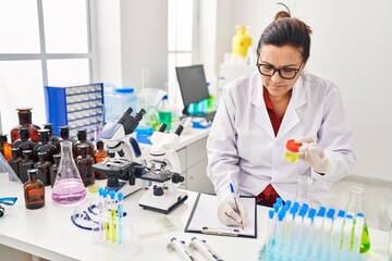 Middle age hispanic woman wearing scientist uniform analysing urine test at laboratory