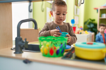 Adorable hispanic boy playing with play kitchen standing at kindergarten