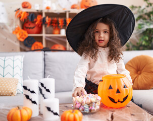 Adorable hispanic girl having halloween party putting sweets on pumpkin basket at home