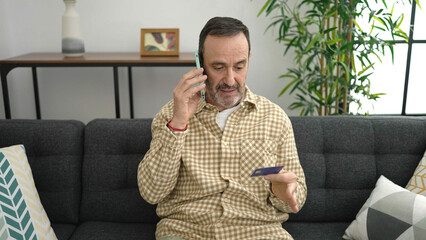 Middle age man talking on smartphone holding credit card at home