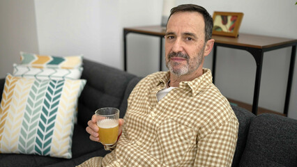 Middle age man holding glass of beer sitting on sofa at home