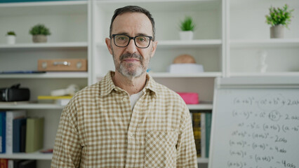 Middle age man teacher standing with serious expression at classroom