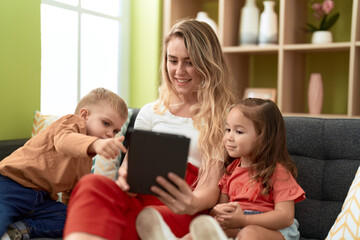 Woman with girl and boy using touchpad sitting on sofa at home