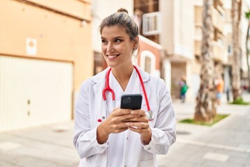 Young blonde woman wearing doctor uniform using smartphone at street