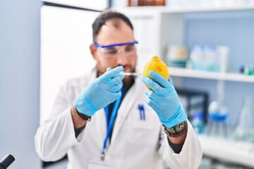 Young hispanic man scientist injecting on lemon at laboratory
