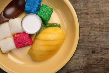 Thai sweet desert red blue yellow white mango sticky rice with coconut cream milk on enamel tin metal plate wood spoon rustic wooden background