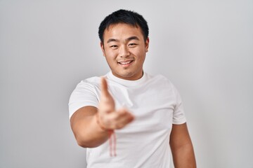 Young chinese man standing over white background smiling cheerful offering palm hand giving assistance and acceptance.