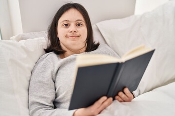 Young woman with down syndrome reading book lying on bed at bedroom