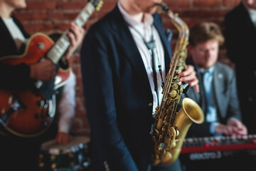 Fototapeta premium Concert view of saxophonist, a saxophone sax player with vocalist and musical band during jazz orchestra show performing music on a stage in the scene lights
