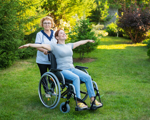 An elderly nurse walks with a middle-aged woman in a wheelchair through the park. The girl spread...